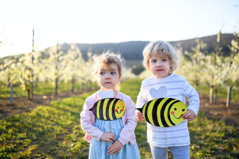 Two small children standing outdoors in orchard in spring, with paper bees